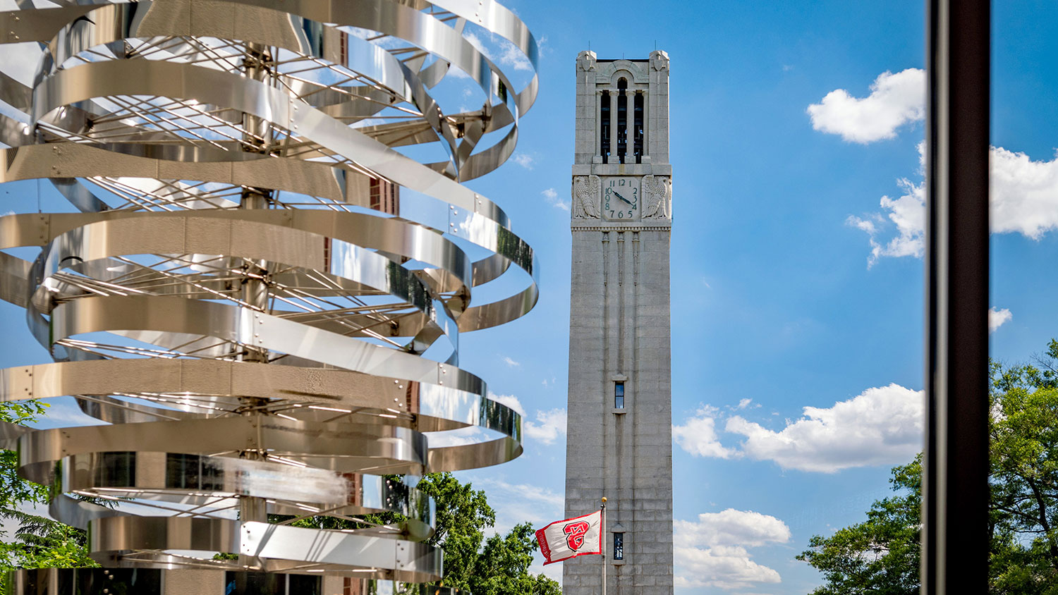 Public art spiral in front of NC State Bell tower and flag